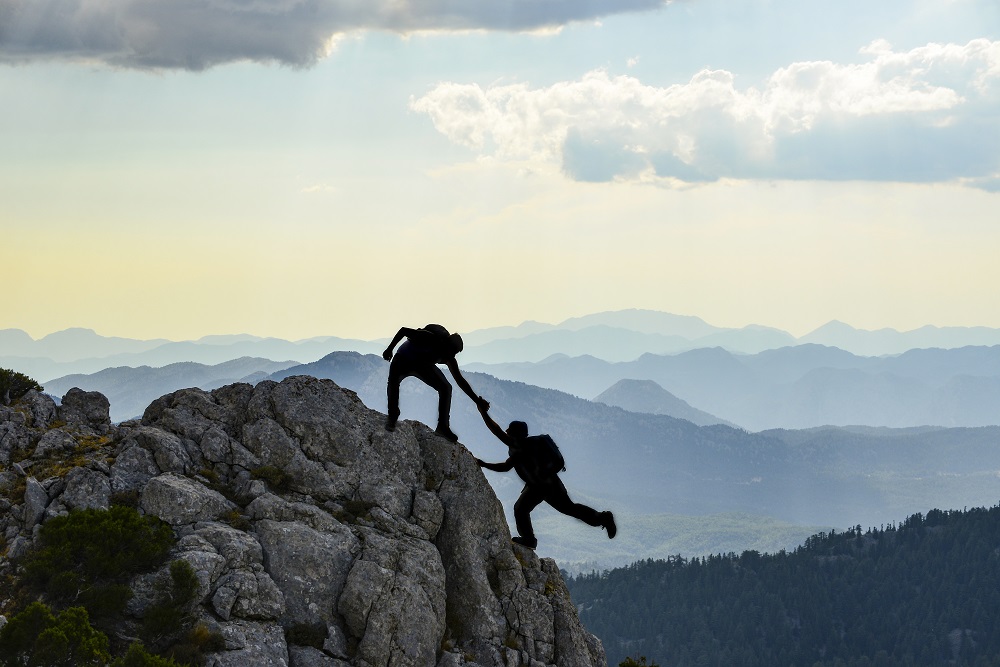 One Person Helping Another To Top Of Mountain. Representing Helping Someone Reach Their Goals