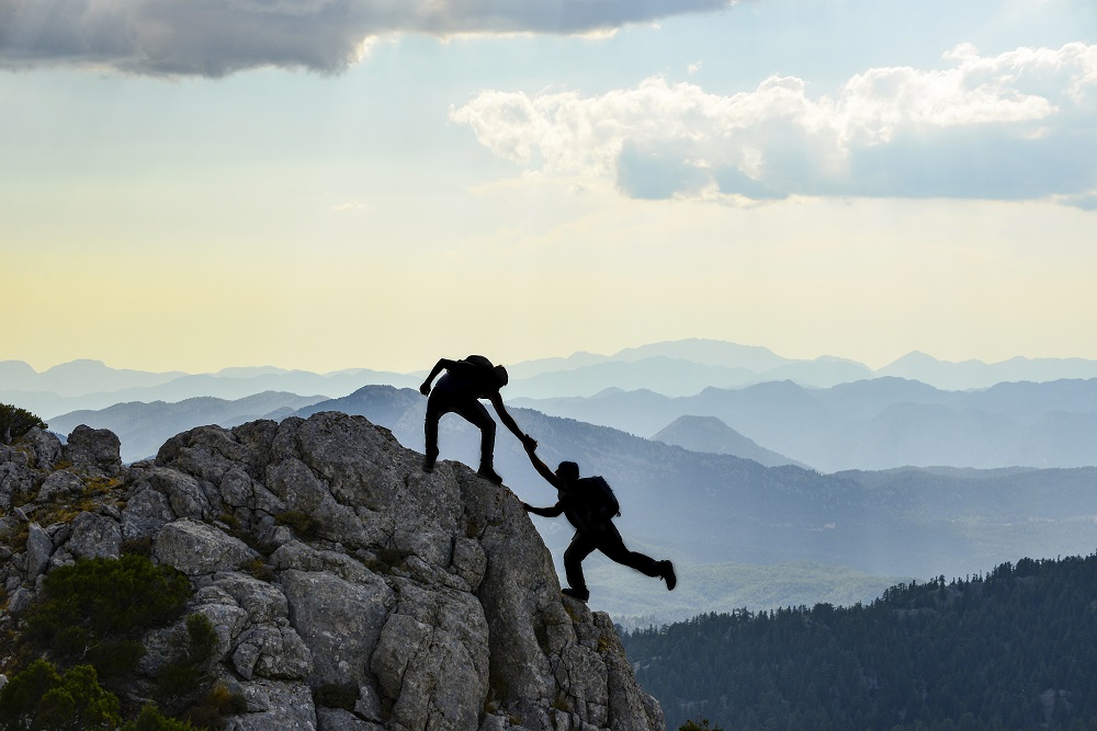 One person helping another to top of mountain ...